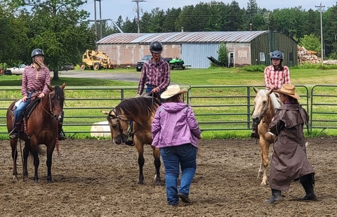 Three older youth members riding horses while two adults look on. 