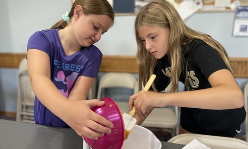 Two girls mixing ingredients in a bowl.