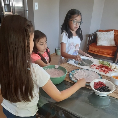 Three young girls make fresh fruit pizza at home